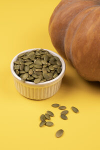 macro-view-bowl-with-many-pumpkin-seeds-yellow-table-close-up-autumn-harvest-concept