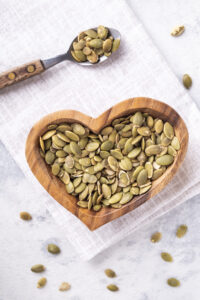 raw-pumpkin-seeds-wooden-bowl-light-background