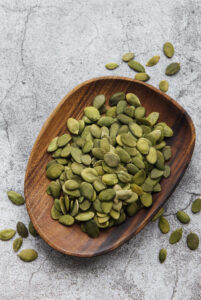 wooden-plate-with-pumpkin-seeds-gray-concrete-background